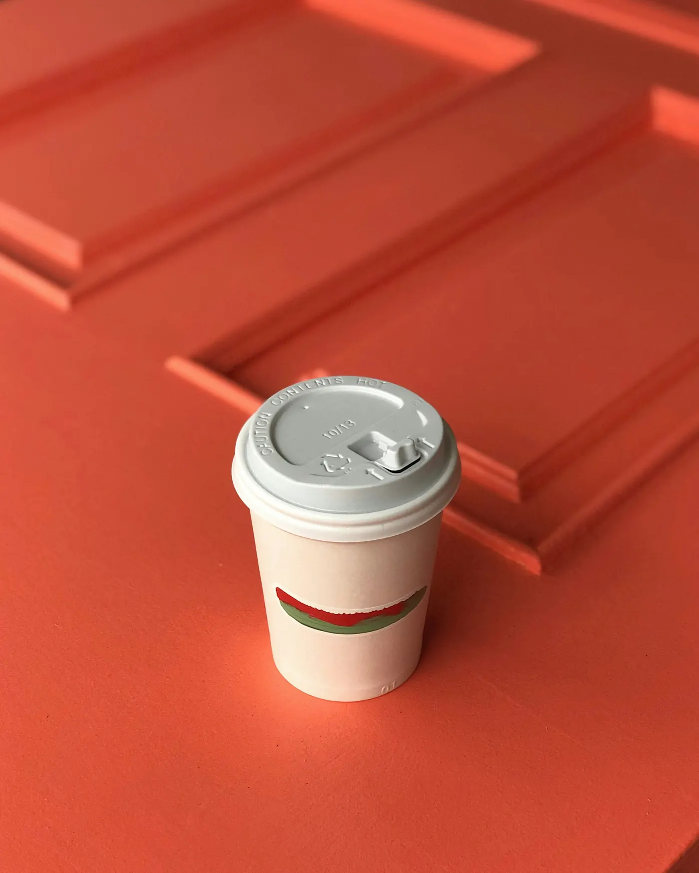 Weißer Coffee-to-go-Becher mit Deckel auf terrakottafarbenem Hintergrund